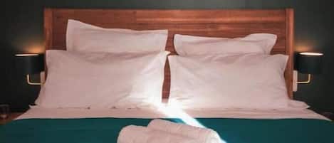 Una cama bien tendida con sábanas blancas y una colcha verde azulada, flanqueada por dos lámparas de noche.