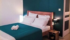 A neatly made bed with white linens and a teal bedspread, a wooden nightstand with a lamp, and a teal accent wall. - Modern Apartment with Sunny Terrace and Sea View (La Possession)