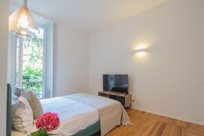 A bedroom with a bed, a TV, and a window with a view of greenery. - Como Liberty Suites - Garbo (Como)