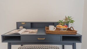 A dark blue desk with a magazine, a cup, a basket with fruits, and a small plant. - Como Liberty Suites - Garbo (Como)