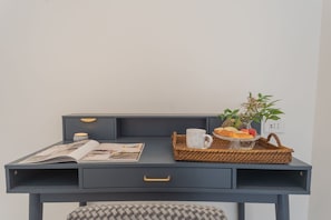 A dark blue desk with a magazine, a cup, a basket with fruits, and a small plant. - Como Liberty Suites - Garbo (Como)