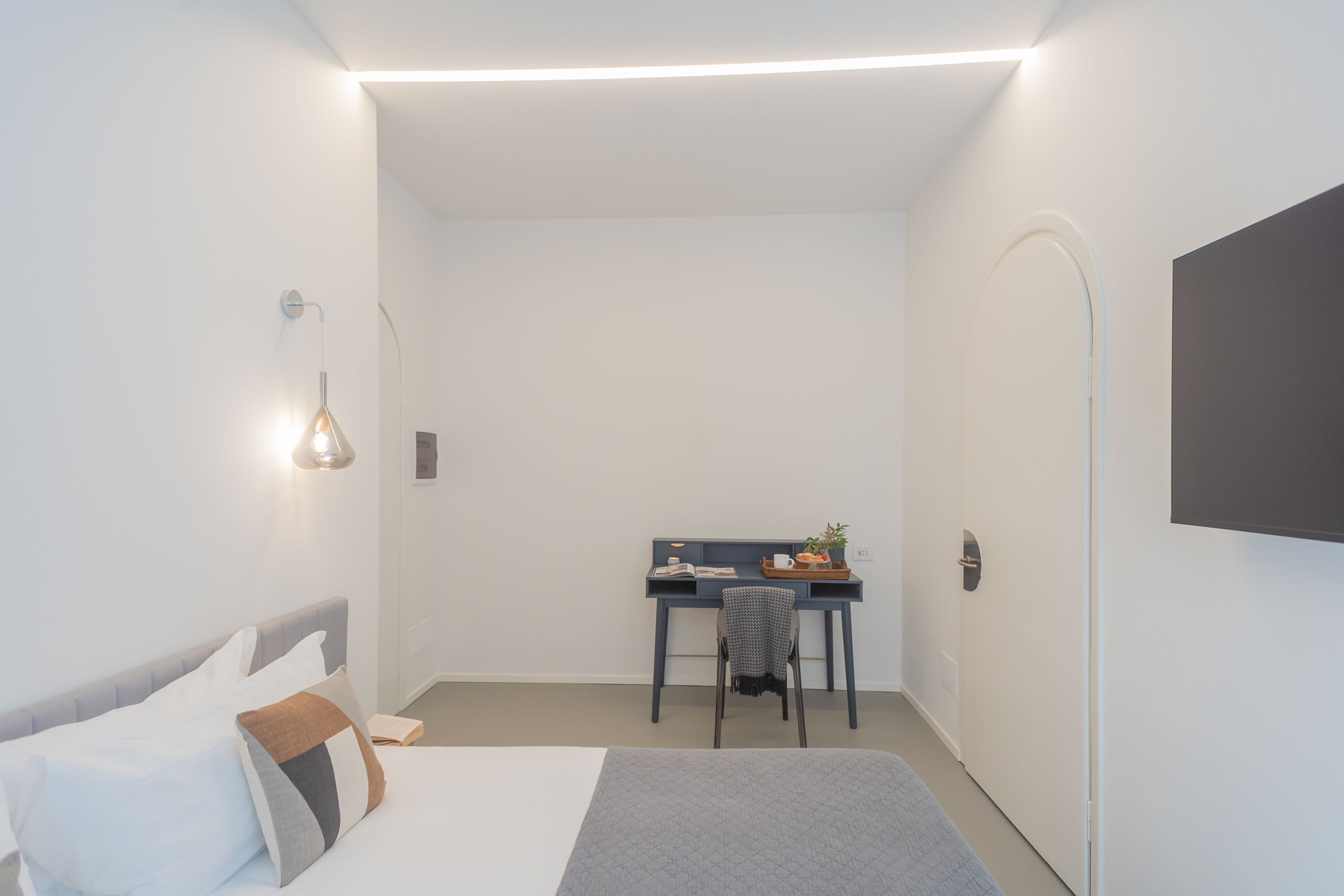 A modern, minimalistic bedroom with a bed, a desk, and a chair.