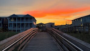 A wooden boardwalk leading to beachfront buildings with a sunset in the background.
