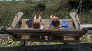 A wooden swing set overlooking a beach with a lifeguard tower in the background.