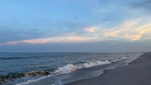 A beach with waves, a pier, and a clear sky.