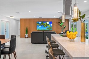 Cozinha moderna com uma ilha grande, área de jantar com cadeiras e sala de estar com sofá.