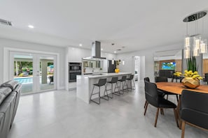 Cozinha moderna com ilha central, banquetas e área de jantar com mesa e cadeiras de madeira.