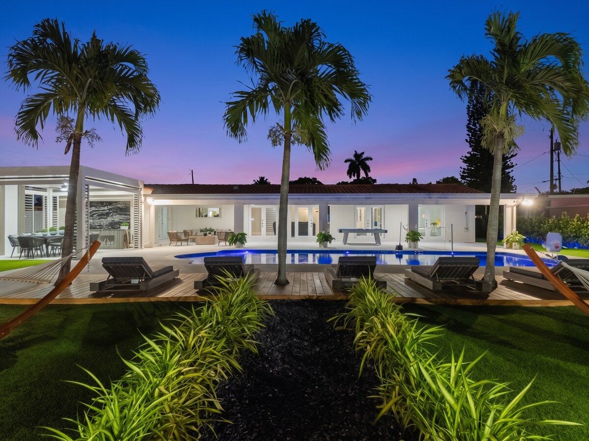 A modern house with a swimming pool, palm trees, and outdoor seating.