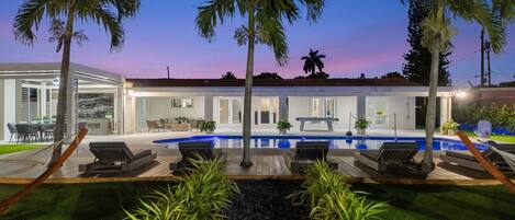 A modern house with a swimming pool, palm trees, and outdoor seating.
