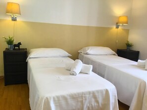 Une chambre d’hôtel avec deux lits simples, du linge de lit blanc, une petite table de chevet avec une lampe et une plante en pot.