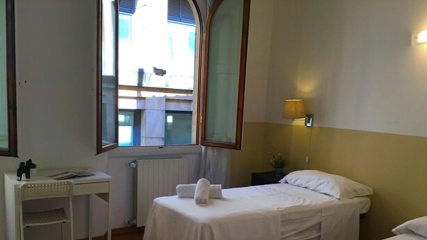 A hotel room with two single beds, a small desk, a chair, a radiator, a window with a view, and a bedside lamp. - Neri 33 in Firenze With 3 Bedrooms and 2 Bathrooms (Florence)