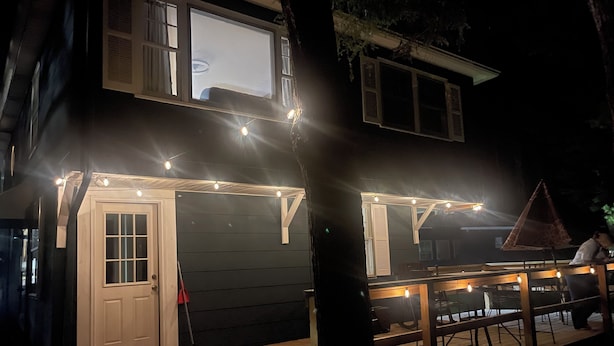 Een tweelaags huis met een terras, lichtjes en een overdekte zitplaats.