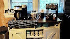 Een aanrecht met koffiezetapparatuur, een koffieteken en een etalage met mokken.