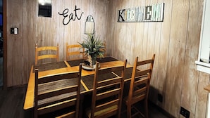 Een eetruimte met een houten tafel en stoelen, een plafondlamp en een muur met de woorden 'eat' en 'kitchen'.