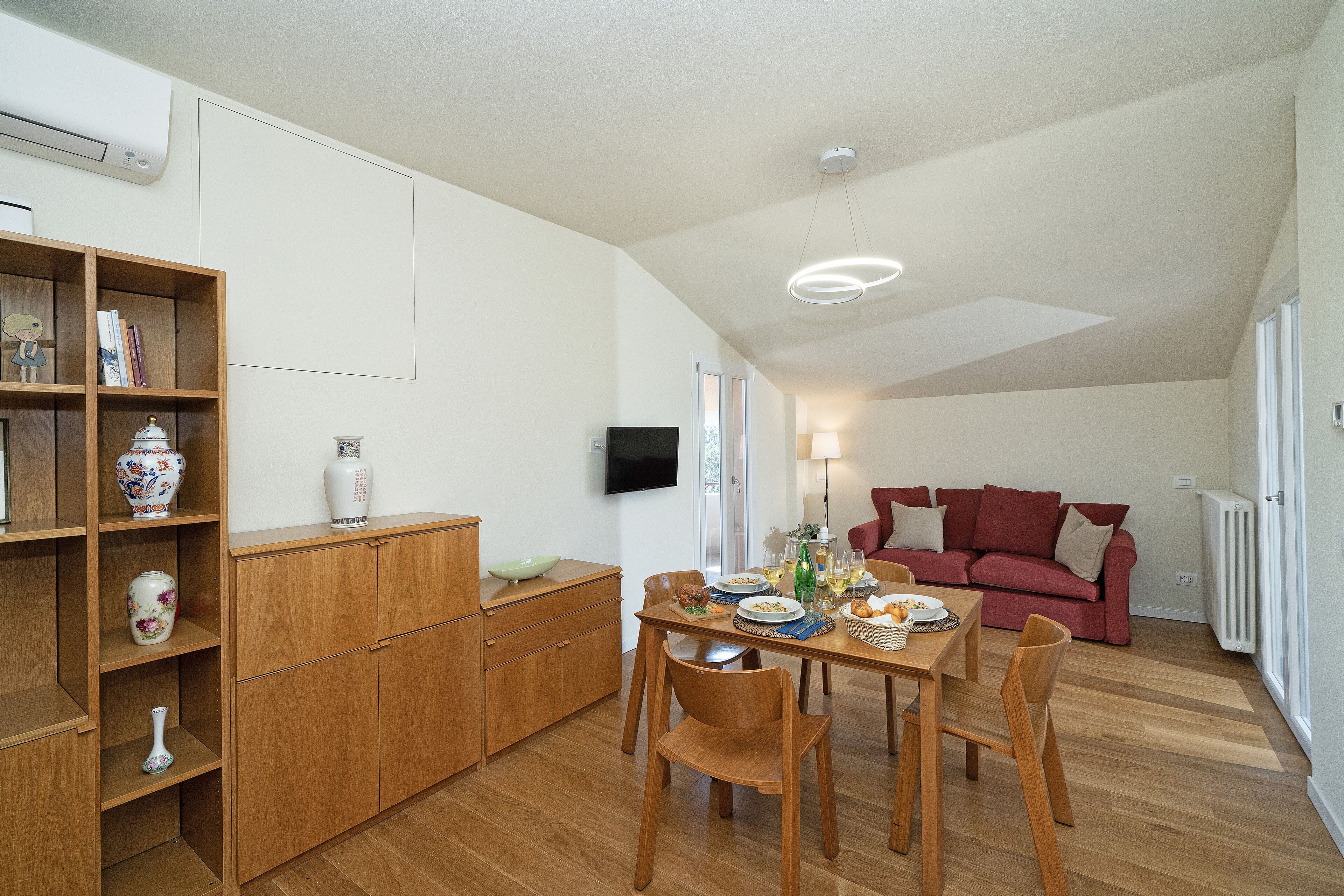 A modern living space with a dining area, a red sofa, wooden furniture, and a flat-screen TV mounted on the wall.