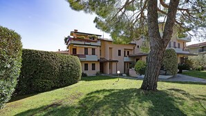 A residential building with a well-maintained lawn, a large tree, and a neatly trimmed hedge.