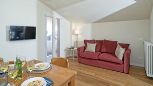 A modern living room with a red sofa, wooden dining table, and a flat-screen TV on the wall.