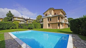 A swimming pool with a stone border, surrounded by a well-maintained lawn and a multi-story building with balconies.