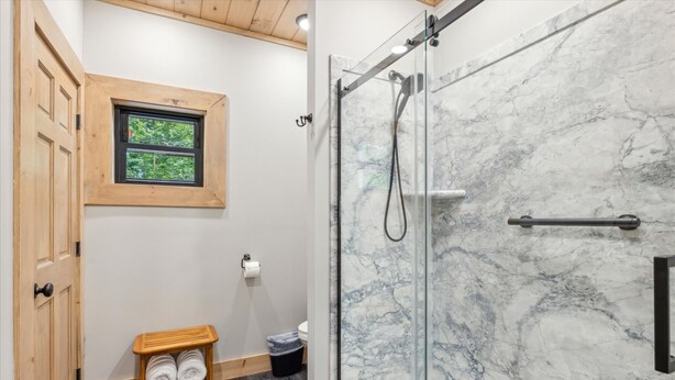 A bathroom with a glass shower enclosure, wooden door, and a small window.