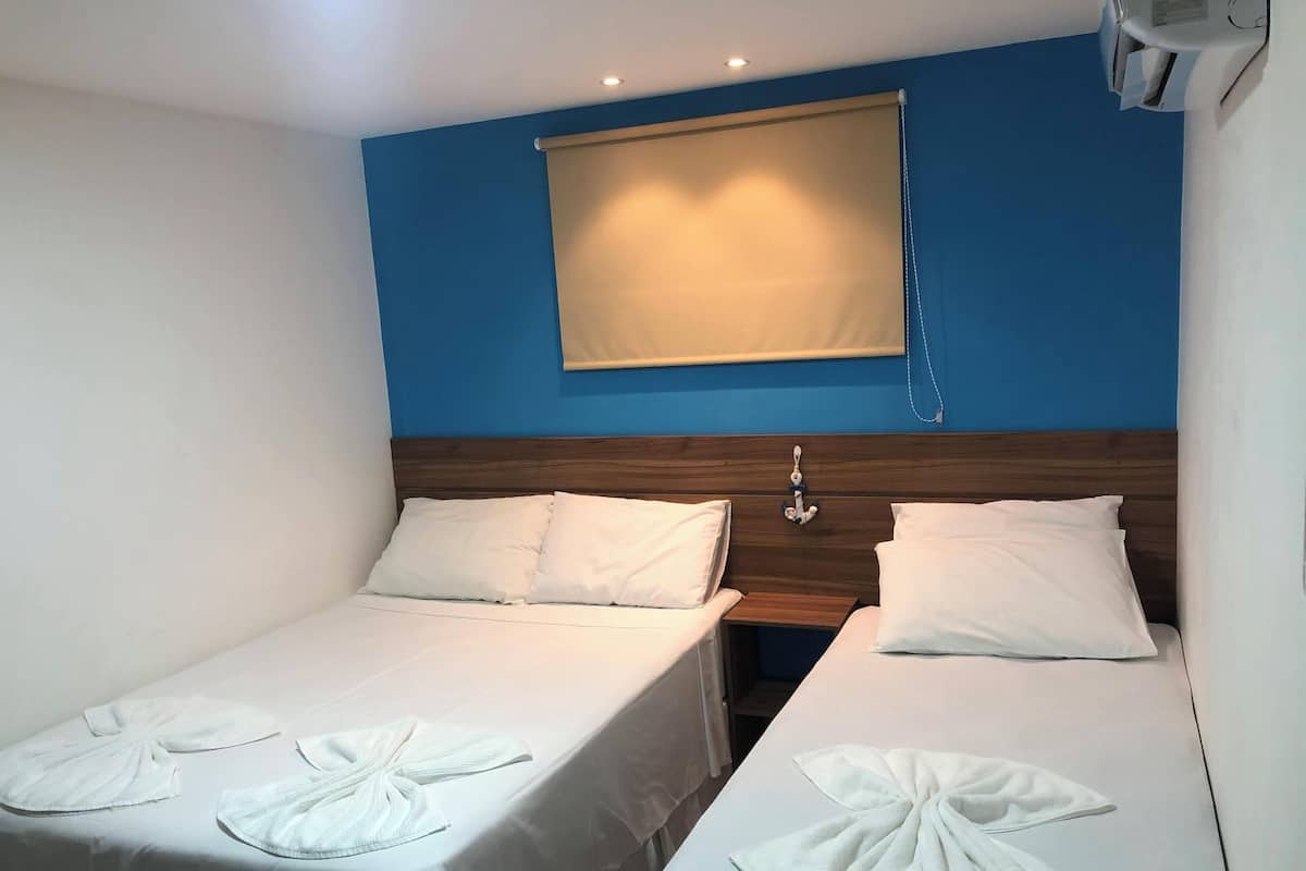 A hotel room with two single beds, a wooden headboard, a beige window blind, and a small bedside table.
