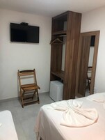 Un dormitorio con una cama, una silla de madera, un televisor montado en la pared y un armario con espejo.