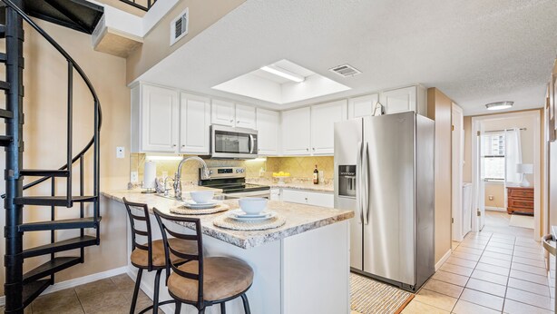 A modern kitchen with white cabinets, stainless steel appliances, a central island with bar stools, and a spiral staircase.