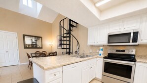 A kitchen with white cabinets, a stainless steel microwave, an oven, a sink, and a staircase.