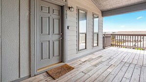 A wooden deck with a gray door, a mailbox, and a view of the beach.