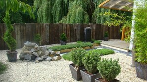 A garden with a wooden fence, a rock feature, and potted plants. - Chambre d'hôte DOLCE VITA + 2-hour access to aqua relaxation area (2 people) (GUSSIGNIES)