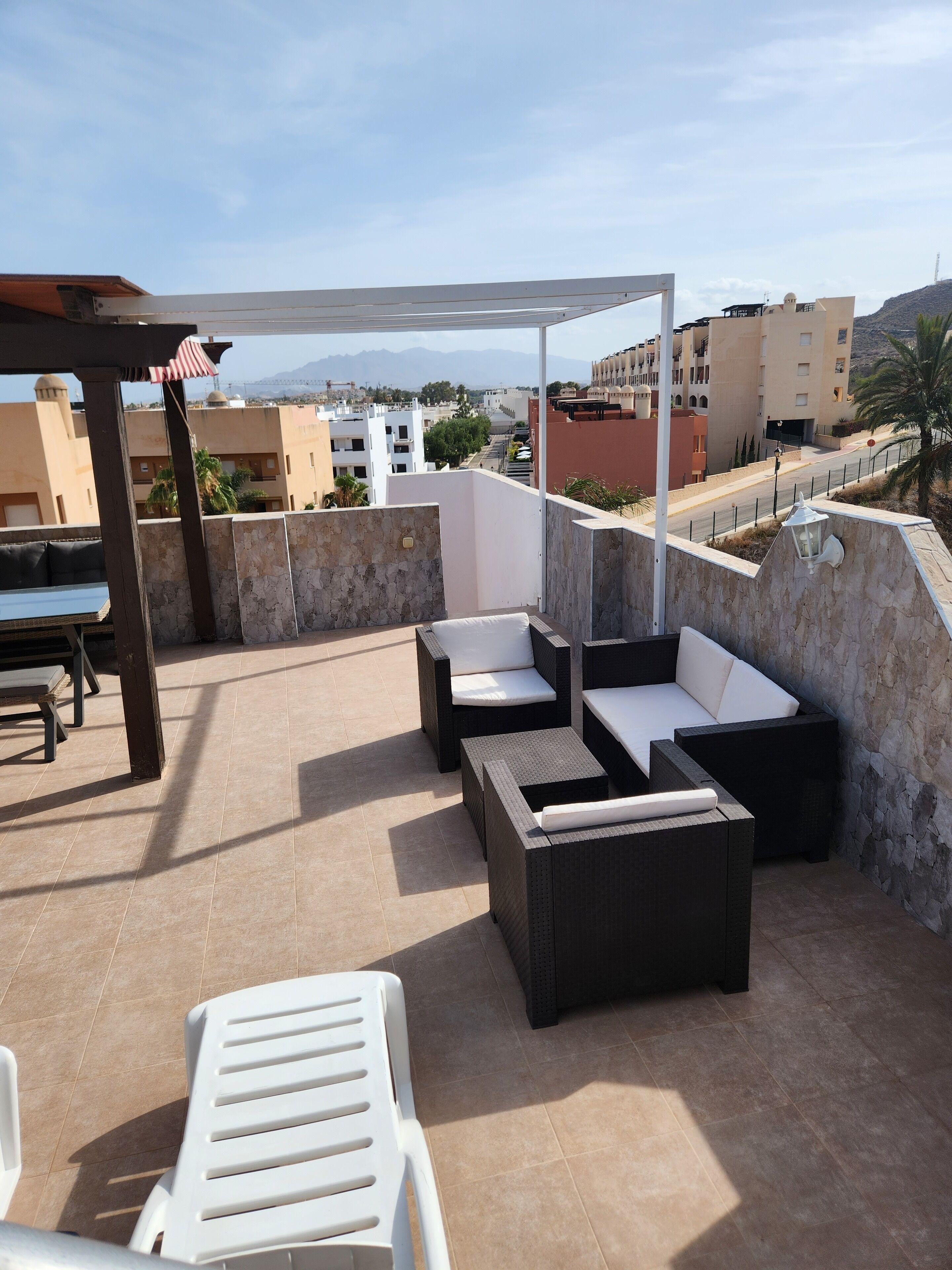 A rooftop terrace with outdoor furniture, a pergola, and a view of the cityscape.