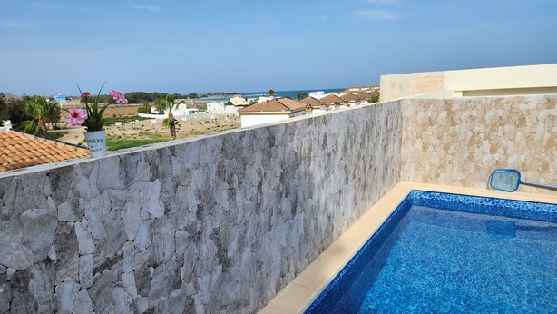 Un mur de pierre avec une piscine et une vue sur une plage et des bâtiments.