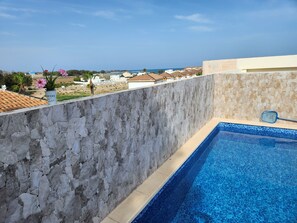 A stone wall with a pool and a view of a beach and buildings. - Ático Precioso muy Luminoso con Piscina Privada! (AN)