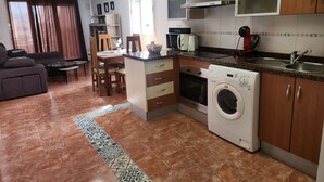 Une cuisine compacte équipée d’un four à micro-ondes, d’un four et d’un lave-linge. Elle comprend également un coin repas avec une table et des chaises.