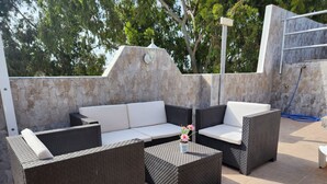 Un espace extérieur aménagé avec un mur en pierre, des meubles en osier et une petite table décorée de fleurs.
