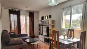 Un salon comprenant un canapé, une table basse en verre, une table à manger avec des chaises, un téléviseur et une étagère décorative.