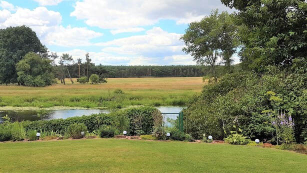 A serene landscape with a pond, lush greenery, and a clear sky. - Spreeblick vacation apartment directly on the old Spree with lots of nature and relaxation (Grünheide)