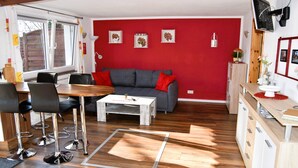 A modern living room with a grey sofa, red cushions, a wooden coffee table, and a red accent wall. - Spreeblick vacation apartment directly on the old Spree with lots of nature and relaxation (Grünheide)
