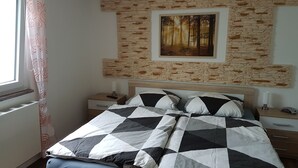 A bedroom with a bed, nightstands, a painting, and a window with curtains. - Spreeblick vacation apartment directly on the old Spree with lots of nature and relaxation (Grünheide)