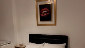 Un lit bien fait, avec du linge de lit blanc, une tête de lit noire et une œuvre d’art encadrée au-dessus.