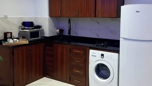 Une cuisine compacte dotée de meubles en bois, d’un four à micro-ondes, d’un lave-linge et d’un réfrigérateur.