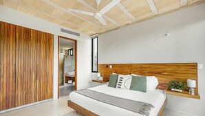 Un dormitorio moderno con cabecera de madera, una cama grande, un ventilador de techo y una mesita de noche con una lámpara y una planta.