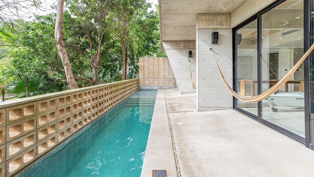 Una piscina con plataforma de concreto, paredes de vidrio y una hamaca.