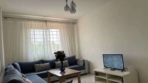 A living room with a sofa, a coffee table, a TV on a stand, and a window with curtains. - Quiet apartment in downtown Agadir (Agadir)
