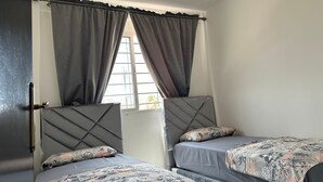 A room with two beds, each with a headboard and a floral-patterned bedspread. There is a window with curtains, and a door is visible on the left side. - Quiet apartment in downtown Agadir (Agadir)