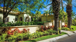 A residential property with a well-maintained garden, palm trees, and a Mediterranean-style house with arched windows and a tiled roof.