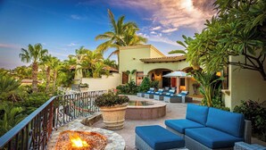 A patio with outdoor seating, a fire pit, and lush greenery.