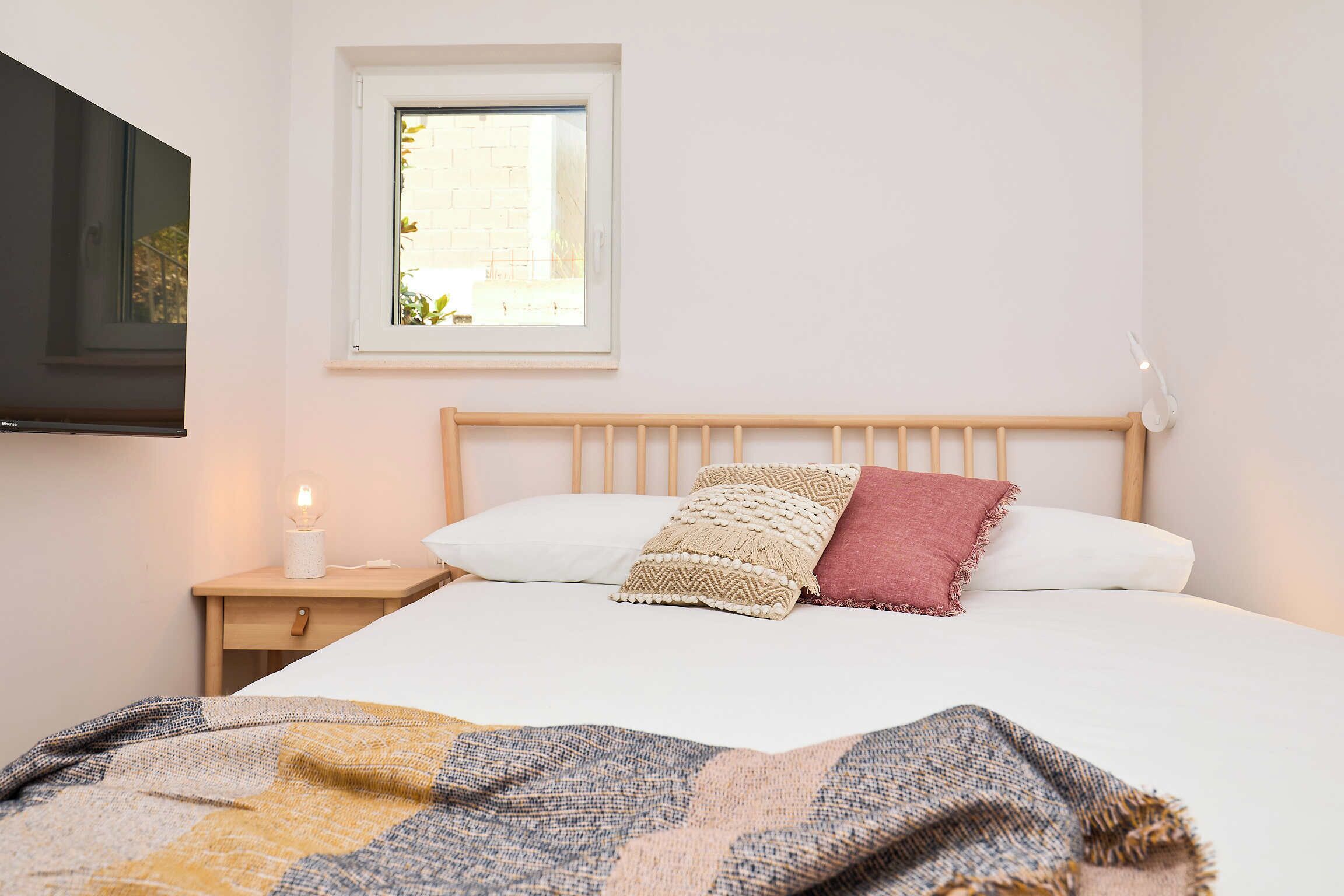 Un lit bien fait, avec une couverture à motifs, une tête de lit en bois et une lampe de chevet.