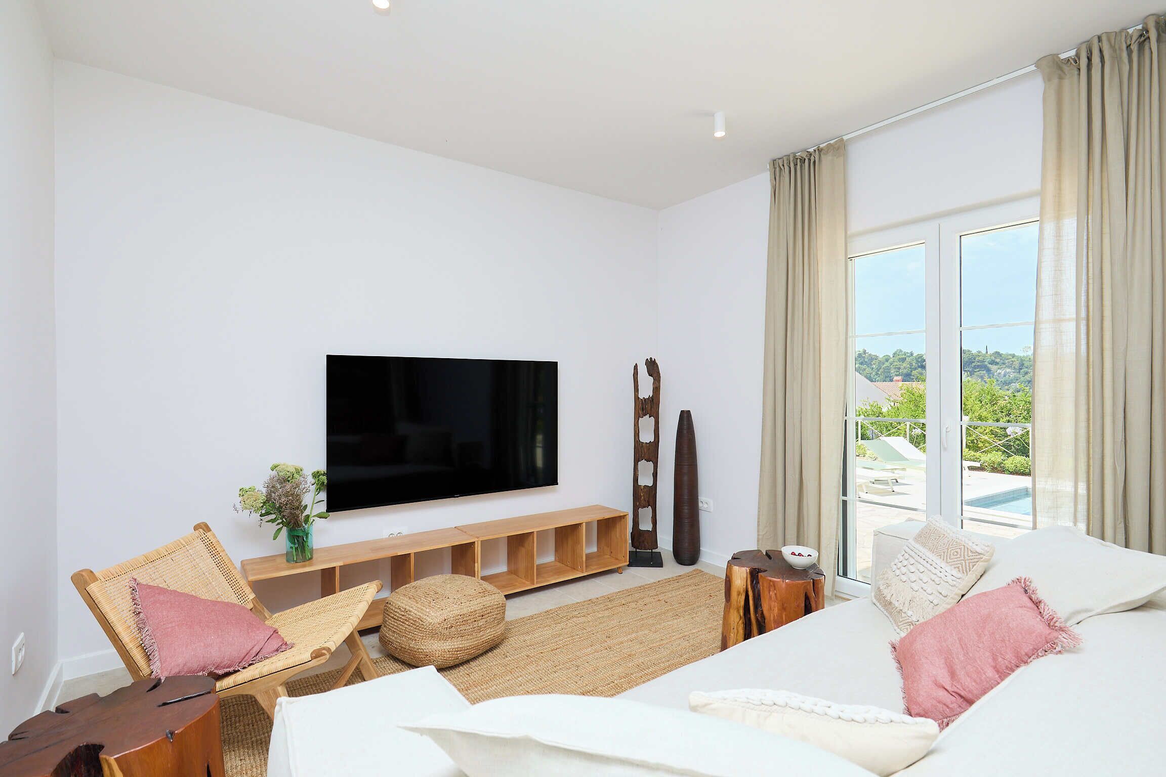 A modern living room with a flat-screen TV, comfortable seating, a large window with a view, and a wooden entertainment unit.