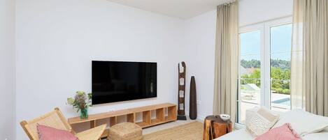 A modern living room with a flat-screen TV, comfortable seating, a large window with a view, and a wooden entertainment unit.