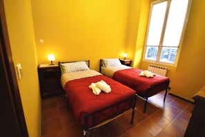 A room with two beds, each with a red bedspread and white pillows, and a window with blinds.